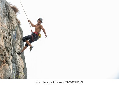 Confidence young Asian man climber with safety rope climbing on rocky mountain at tropical island in sunny day. Strong handsome male enjoy outdoor active lifestyle and extreme sport on summer vacation - Powered by Shutterstock