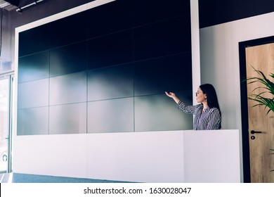 Confident Adult Woman In Elegant Clothes Presenting Project While Focusing And Pointing Hand On Big Empty Screen In Office Conference Room