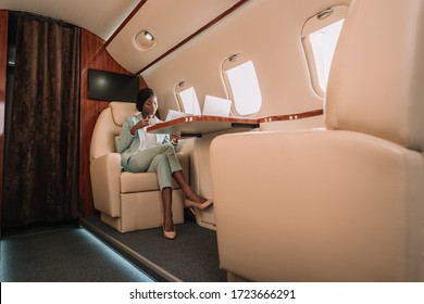 confident african american businesswoman drinking coffee and reading newspaper in private jet