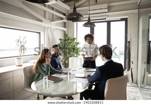 Confident African American businesswoman leading\
briefing, explaining strategy, training diverse staff sitting at\
table in boardroom, group negotiations, business partners sharing\
startup ideas