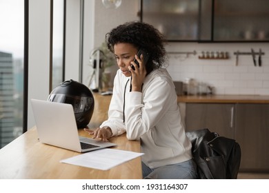 Confident African American businesswoman making phone call, using laptop, searching information, consulting client, negotiating with business partner, sitting at table with motorcycle helmet