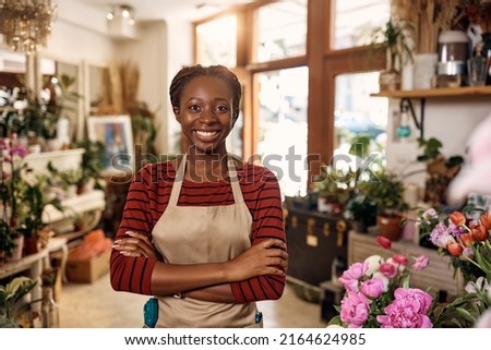Confident African American female florist with crossed arms at flower shop looking at camera.