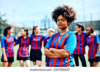 Confident African American female soccer player at the stadium looking at camera. Her teammates are in the background. - Powered by Shutterstock