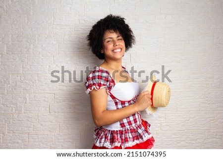 Confident african american girl with curly hair wearing traditional junina costume holding hat with big smile. Brazilian June Party, typical celebration in Brazil.