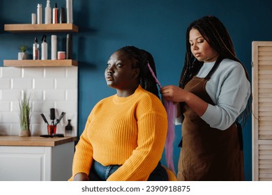 Confident African American hairdresser braiding hair to a female customer in salon - Powered by Shutterstock