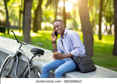 Confident African American Man With Bicycle And Coffee Having Conversation On Mobile Phone At City Park