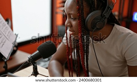 Confident african american woman reporter in braids, speaking on air at an indoor music studio, broadcasting news via radio, with headphones on