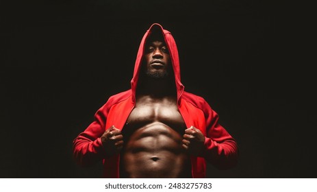 Confident african bodybuilder in red hooded shirt with bare chest, black studio background - Powered by Shutterstock