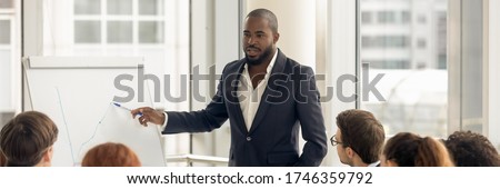 Confident African business coach gives presentation on flip chart, consults clients, teach employees, explain corporate strategy at seminar concept. Horizontal photo banner for website header design
