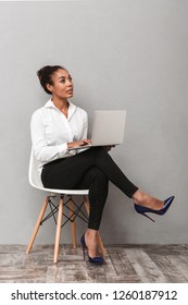 Confident African Business Woman Wearing Suit Sitting In A Chair, Using Laptop Computer Over Gray