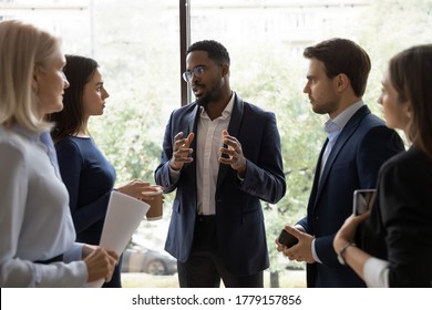 Confident African Male Leader Standing Telling Diverse Colleagues About New Project, Boss Lead Briefing For Different Age Workgroup Team Employees In Office. Sharing Information And Leadership Concept