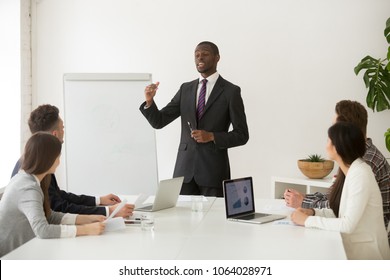 Confident African Speaker Business Coach In Suit Giving Presentation Training Sales Team In Office, Black Businessman Speaking At Seminar Teaching People Group Presenting New Marketing Project Goals