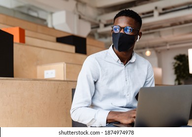 Confident african student wearing medical mask standing in the classroom, holding laptop - Powered by Shutterstock