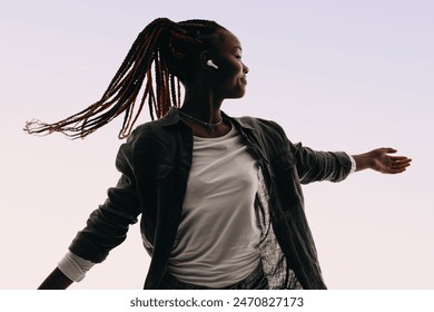 Confident African woman celebrates her vibrant lifestyle with expressive dancing in a studio. Listening wirelessly on earbuds, she embodies the fun of Gen Z, flowing to the rhythm with joy. - Powered by Shutterstock