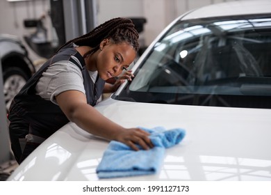 Confident African Woman Holds Blue Microfiber In Hand And Polishes The Car. Cleaning Washing Auto. Side View Portrait Of Young Black Auto Mechanic Woman In Uniform At Work In Car Service