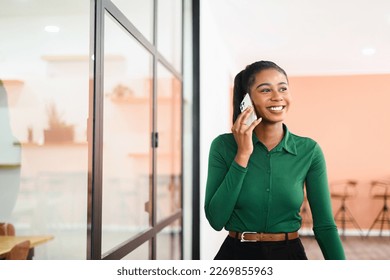 Confident African-American businesswoman talks phone walking down office hall, cheerful friendly female employee speaks on mobile phone with clients, chatting on smartphone - Powered by Shutterstock