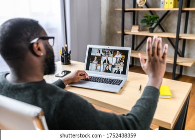 Confident African-American male worker talking online with coworkers, back view of black guy is waving hello to many people on video screen. Remote work, virtual meeting