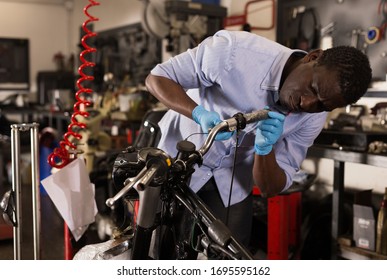 Confident afro american worker using his tools for repairing in motorcycle workshop