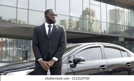 Confident Afro-American driver standing by car, security guard service, business