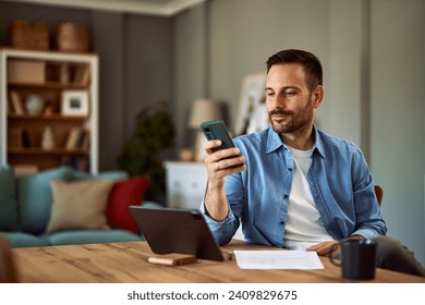 A confident and ambitious male freelancer scrolling through social media on his smartphone, while on his break and sitting in front of a tablet for his work. - Powered by Shutterstock