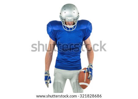 Confident American football player looking down while holding ball against white background