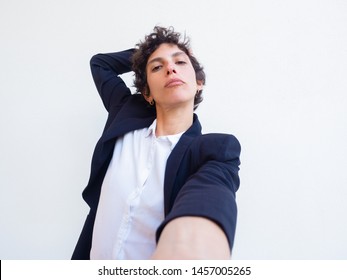 Confident Androgynous Young Woman Holding Cell Phone In Hand And Taking Selfie. Self Portrait Of Female Professional In Office Suit. Poser Concept