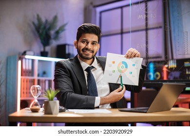 Confident Arab Financial Expert Office Worker In Suit Working On Laptop, Showing Paper Report With Graphs And Charts During Video Meeting With Colleagues In Office.