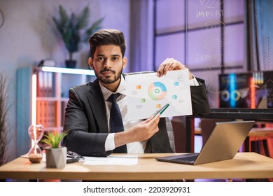 Confident Arab Financial Expert Office Worker In Suit Working On Laptop, Showing Paper Report With Graphs And Charts During Video Meeting With Colleagues In Office.