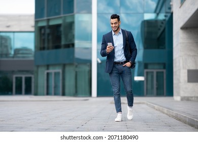 Confident Arabic Guy Programmer With Backpack Walking By Street, Checking His Mobile Phone, Chatting With Friends, Going Home From Office, Panorama With Copy Space, Full Length