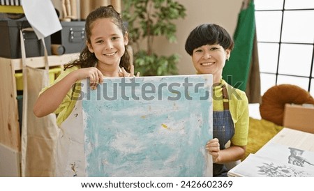 Confident art teacher and student showoff their canvas drawing, smiling together in the cozy studio