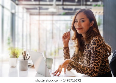 Confident asian businesswoman smiling and look at camera while working on laptop at modern office. Woman laptop working concept