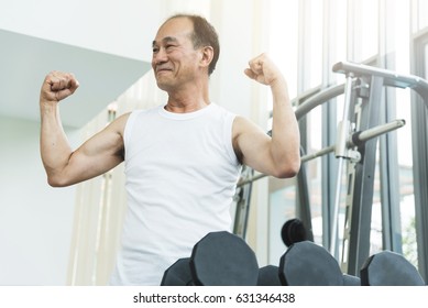 Confident Asian Elderly Man Showing Muscle Arms During Workout At The Gym. Happy Smiling Senior Male Exercise. Copy Space.