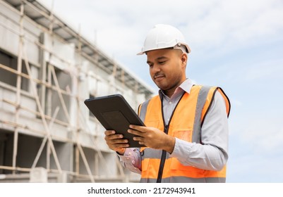 Confident Asian Engineer Man Using Tablet For Checking And Maintenance To Inspection At Modern Home Building Construction. Architect Working With White Safety Helmet In Construction Site