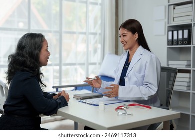 Confident Asian female doctor explains and questions a retired female patient attending a private clinic for treatment and therapy. Health concept, health insurance. - Powered by Shutterstock