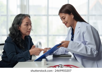 Confident Asian female doctor explains and questions a retired female patient attending a private clinic for treatment and therapy. Health concept, health insurance. - Powered by Shutterstock