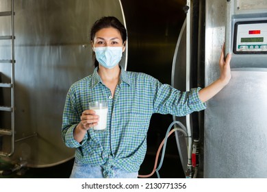 Confident Asian Female Milker In Protective Face Mask Posing With Glass Of Milk At The Cow Farm