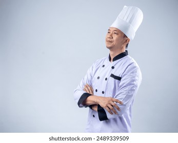 A confident Asian male chef in a white uniform and hat, standing with arms crossed and smiling, exudes professionalism and expertise against a light blue background - Powered by Shutterstock