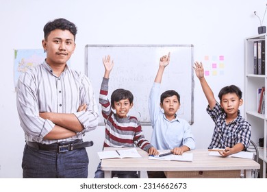 Confident Asian male teacher standing in front of schoolboy who raising their hands and looking at camera. Banner for Teacher's Day. - Powered by Shutterstock