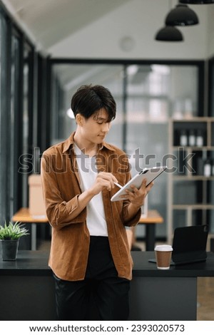 Confident Asian man with a smile standing holding notepad and tablet at the modern office.