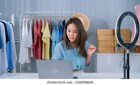 Confident Asian Online Shopkeeper Talking With Customers In Live Streaming On Mobile Phone Showing New Collections At Fashion House Clothes Store Making Free Shipping In Online Shopping