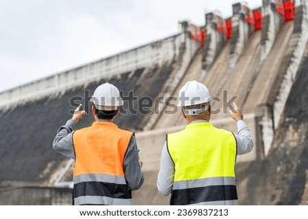 Confident asian two maintenance engineers man inspection discussstion with tablet at construction site dam with hydroelectric power plant and irrigation. Team engineer man working at project