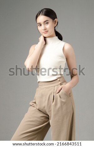 Confident Asian woman puts her hands in pocket and looks at the camera isolated over grey background. Portrait of pretty girl in studio.