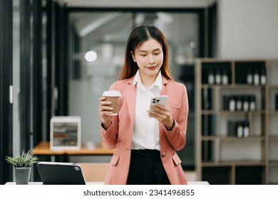 Confident Asian woman with a smile standing holding notepad and tablet at the modern office.
