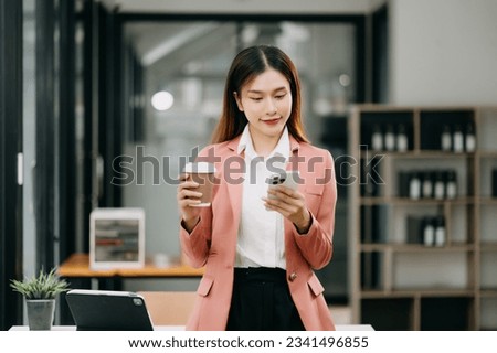 Confident Asian woman with a smile standing holding notepad and tablet at the modern office.

