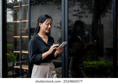 A confident, attractive Asian businesswoman is reading text messages or replying to chats on her smartphone while walking through an office corridor. people and wireless technology concepts - Powered by Shutterstock