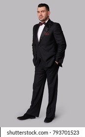 Confident Attractive Young Man In Tuxedo Standing With Hand In Pocket. Full Body. Studio Isolated