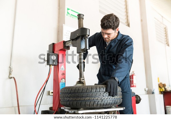 Confident auto expert in coveralls using tire\
changer machine at repair\
shop