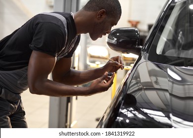 confident auto mechanic man using brush for painting a car, applying paint of black representative automobile after scratching
