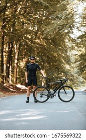 Confident Bearded Cyclist In Special Sport Outfit Standing Near His Black Bike And Looking At Camera. Mature Man In Protective Helmet And Mirrored Glasses Enjoying Workout Outdoors.