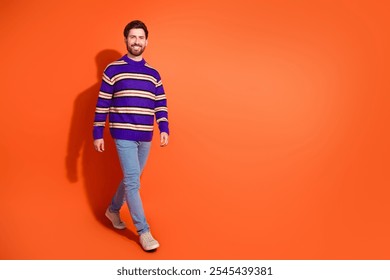 Confident bearded man in a striped sweater walking across orange backdrop, exuding style and positivity - Powered by Shutterstock